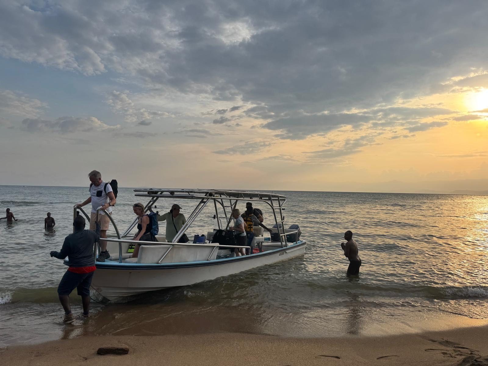 Reizigers stappen uit een boot op het strand van Lake Kivu bij zonsondergang